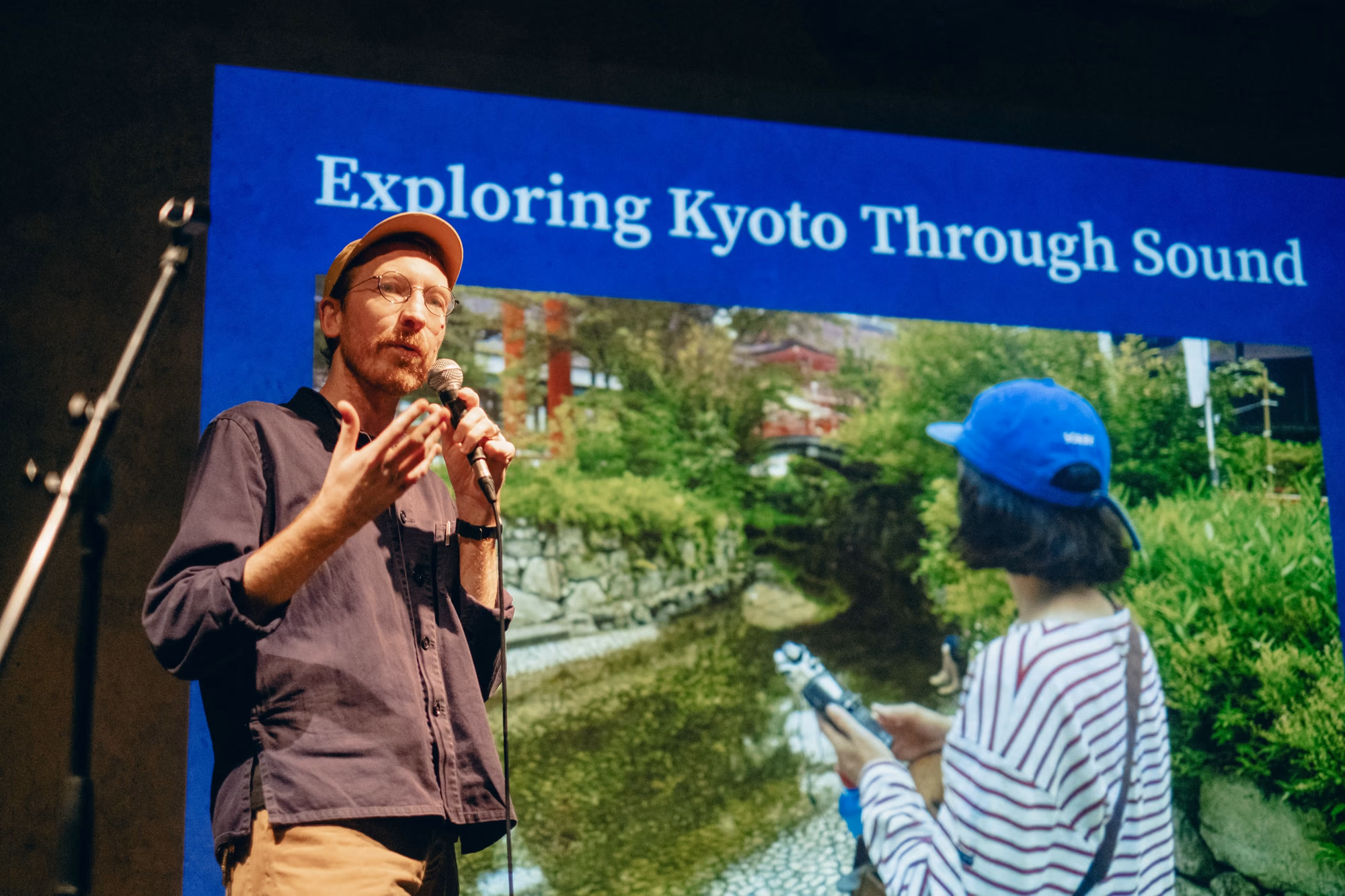 Simon James French speaking on stage at Pecha Kucha Kyoto, in front of a slide reading Exploring Kyoto Through Sound